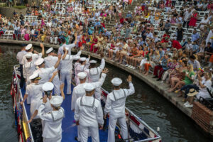 Commander, Naval Medical Forces Support Command joined by commanding officer, Navy Medical Research Unit San Antonio and Sailors and Coast Guardsmen representing the Sea Services wave to the crowd during the Texas Cavaliers Fiesta River Parade June 21, 2021, San Antonio, Texas. The parade is one of key events during Fiesta San Antonio and dates back to 1941. It runs along the River Walk in downtown San Antonio. Fiesta began as a one-time parade (Battle of Flowers) in 1891, to honor the memory of the heroes of the Alamo and the Battle of San Jacinto, has grown into a celebration of San Antonio's rich and diverse cultures. Military representatives participate in receptions, parades, pilgrimages and memorials. (Air Force photo by Mr. Johnny Saldivar.)