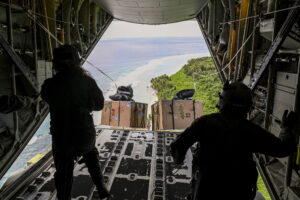 U.S. Air Force loadmasters assigned to the 36th Airlift Squadron, Yokota Air Base, Japan, watch as bundles fly off an aircraft during Operation Christmas Drop at Andersen Air Force Base, Guam, Dec. 10, 2021. Over the course of 10 days, crews airdropped donated food, clothing, educational materials, and tools to 55 islanders throughout the South-Eastern Pacific, including the Federated States of Micronesia, and the Republic of Palau. (U.S. Air Force photo by Senior Airman Aubree Owens.)