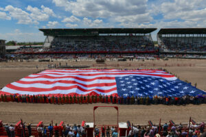Airmen and families hold the American flag for the national anthem during Military Monday at Cheyenne Frontier Days, July 23, 2022, at the Cheyenne Rodeo Grounds. Fort D.A. Russell and F.E Warren Air Force Base have supported Cheyenne Frontier Days since its inception in 1897, and CFD continues to honor the military by dedicating a day to all service members. (U.S. Air Force photo by Airman 1st Class Sarah Post.)