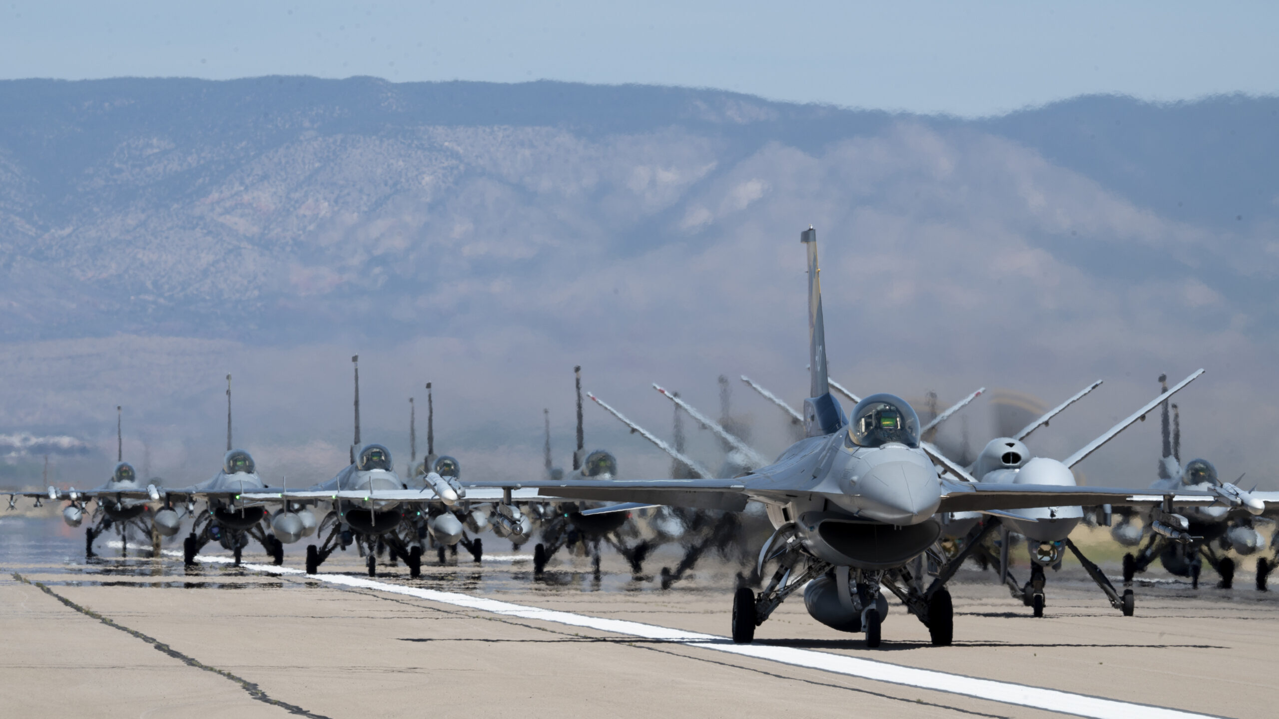 Forty-nine F-16 Vipers and MQ-9 Reapers assigned to the 49th Wing line up on the runway during an elephant walk at Holloman Air Force Base, N.M., April 21, 2023. The 49th Wing is the Air Force’s largest F-16 and MQ-9 formal training unit, building combat aircrew pilots and sensor operators ready for any future conflicts. (U.S. Air Force photo by TSgt Victor J. Caputo.)