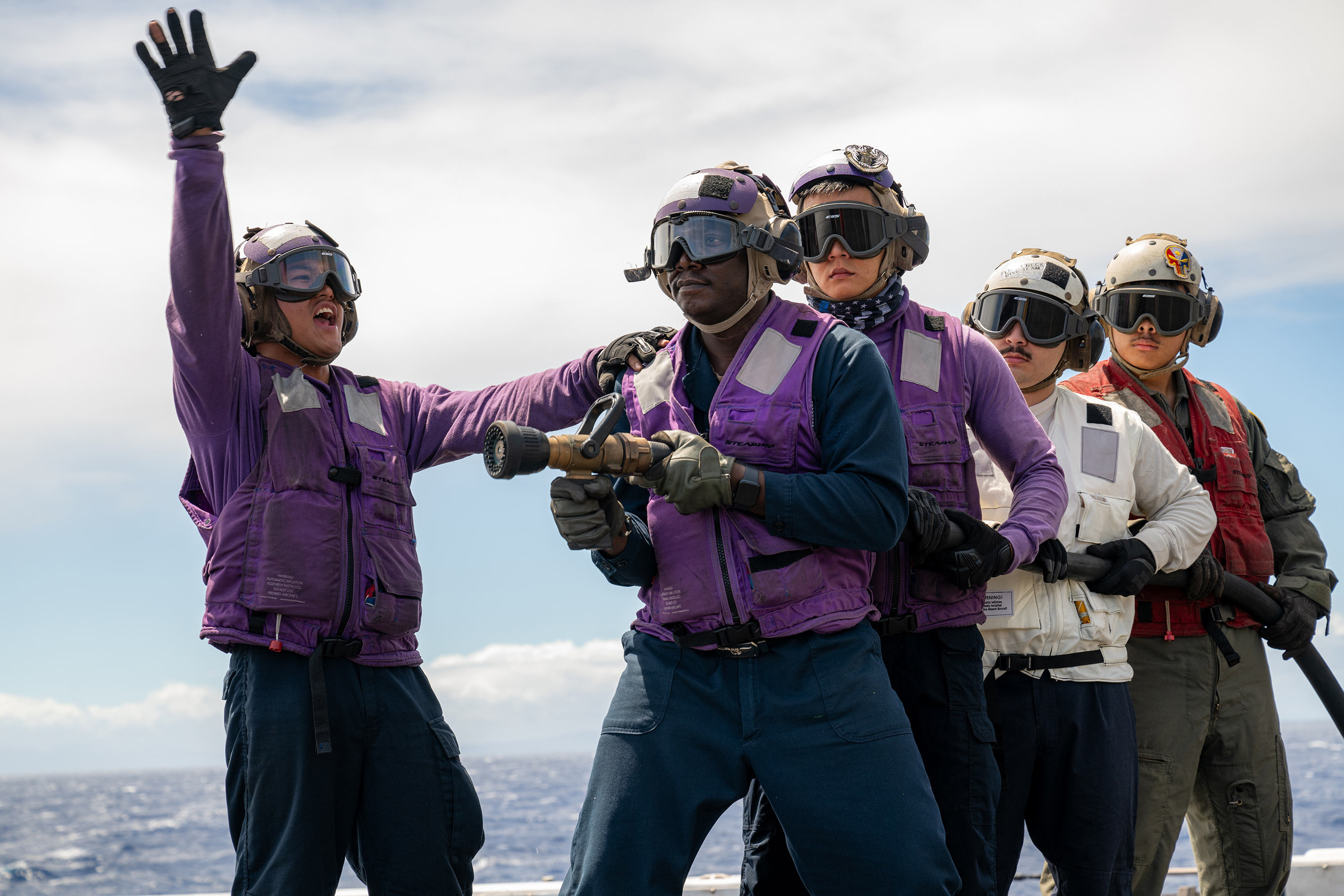Aviation Boatswain's Mate (Fuels) Airman Apprentice (left), a Wapato, Washington native, signals to a scene leader during a crash and salvage drill on the flight deck of the San Antonio-class amphibious transport dock ship USS Somerset (LPD 25) during Exercise Rim of the Pacific 2024 while underway in the Pacific Ocean, July 27. Twenty-nine nations, 40 surface ships, three submarines, 14 national land forces, more than 150 aircraft and 25,000 personnel are participating in RIMPAC in and around the Hawaiian Islands, June 27 to Aug. 1. The world's largest international maritime exercise, RIMPAC provides a unique training opportunity while fostering and sustaining cooperative relationships among participants critical to ensuring the safety of sea lanes and security on the world's oceans. RIMPAC 2024 is the 29th exercise in the series that began in 1971. (U.S. Navy photo by Mass Communication Specialist 2nd Class Evan Diaz.)