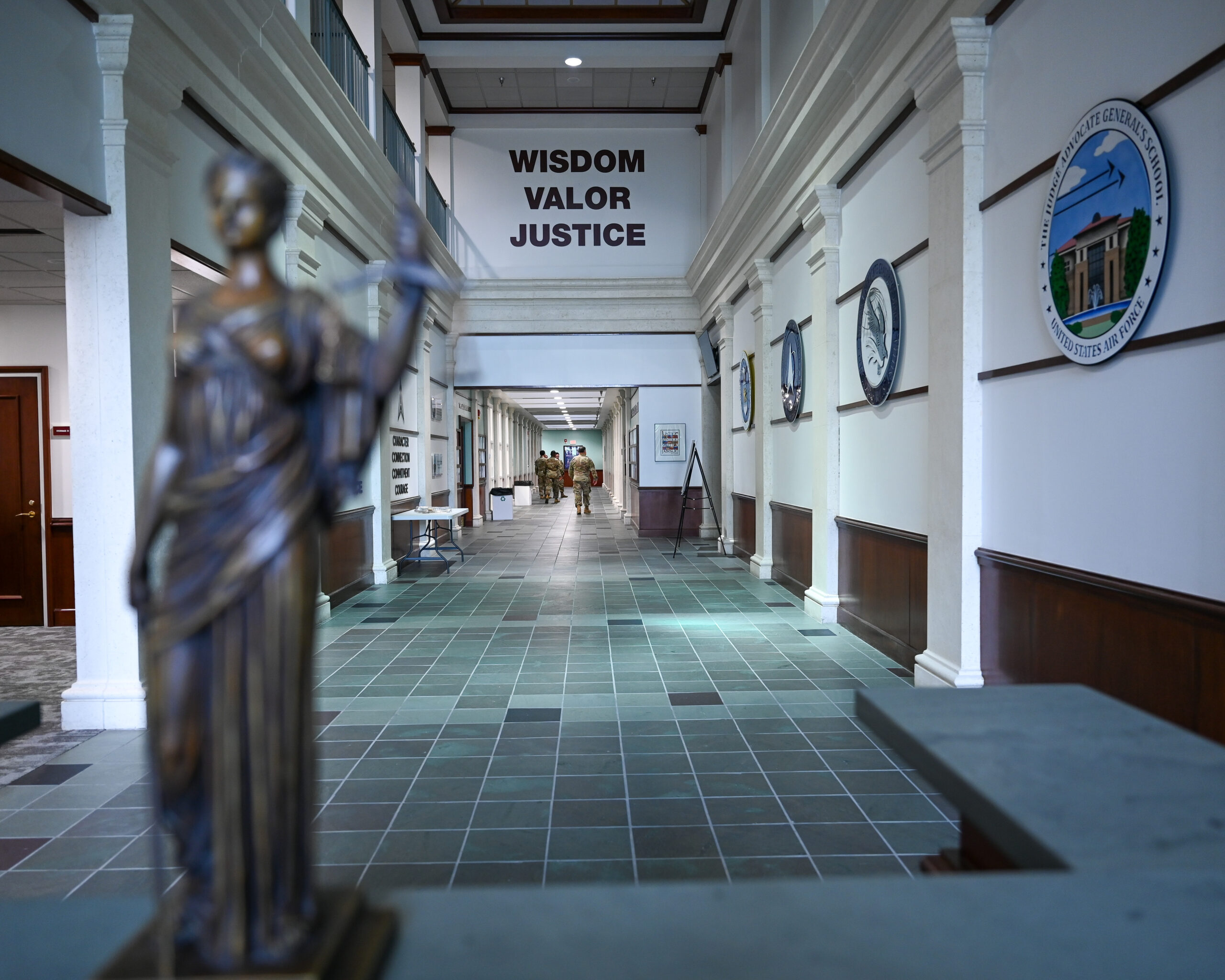 Airmen walk through the main corridor of the Judge Advocate General’s School at Maxwell Air Force Base, Alabama, June 5, 2025. The words “Wisdom, Valor, Justice” are displayed on the wall, embodying the core values of the U.S. Air Force Judge Advocate General’s Corps as they prepare military legal professionals to uphold the Constitution and the rule of law. (U.S. Air Force photo by Airman 1st Class Nelvis Sera.)